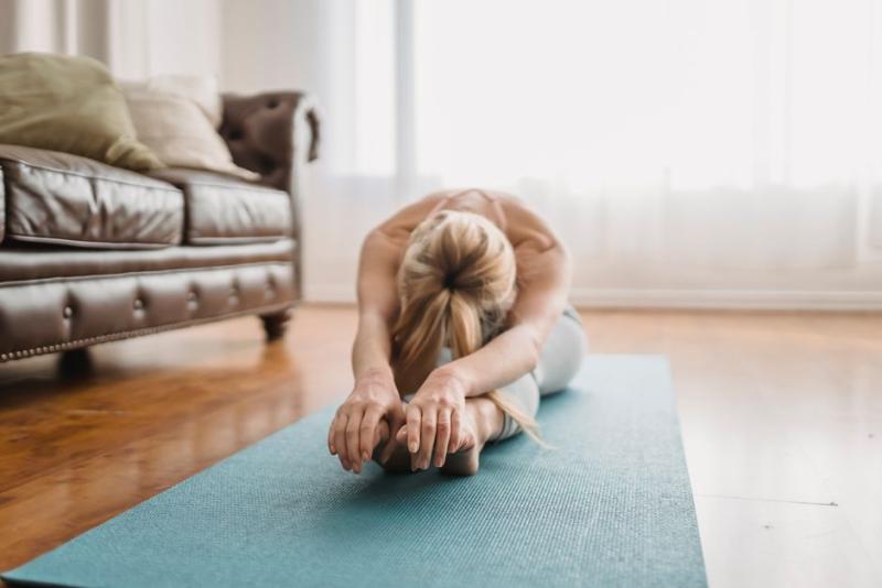 Mujer haciendo estiramiento de pilates sobre esterilla en el salón de casa