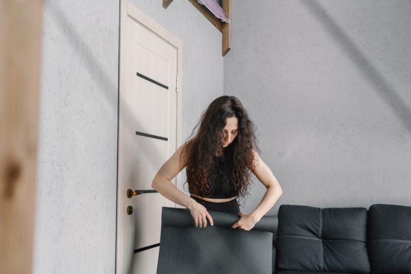 Mujer desenrollando su esterilla en casa para empezar su sesión de pilates