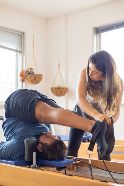 Instructora corrigiendo la postura de la pierna de un alumno en el reformer