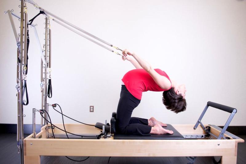 Mujer haciendo un estiramiento de columna en reformer de pilates