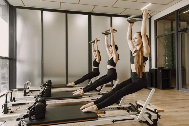 Grupo practicando pilates reformer con los brazos elevados sujetando un aro
